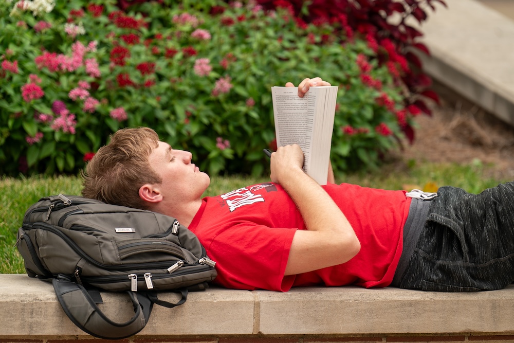 student laying down on campus and reading a book