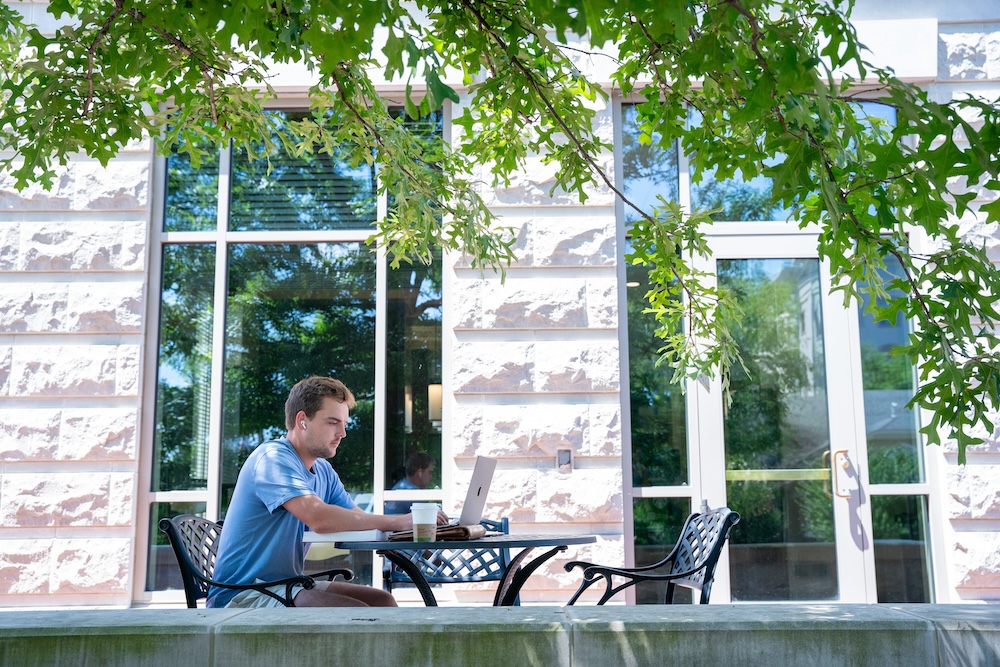 student studying at an outdoor table with laptop