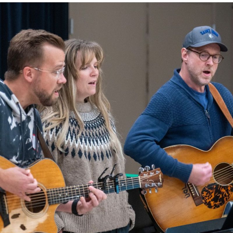 Three singers perform in front of a microphone