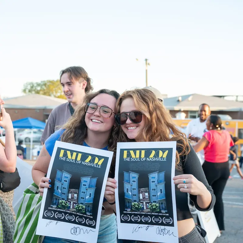 two girls smiling holding up posters for "Exit 207"