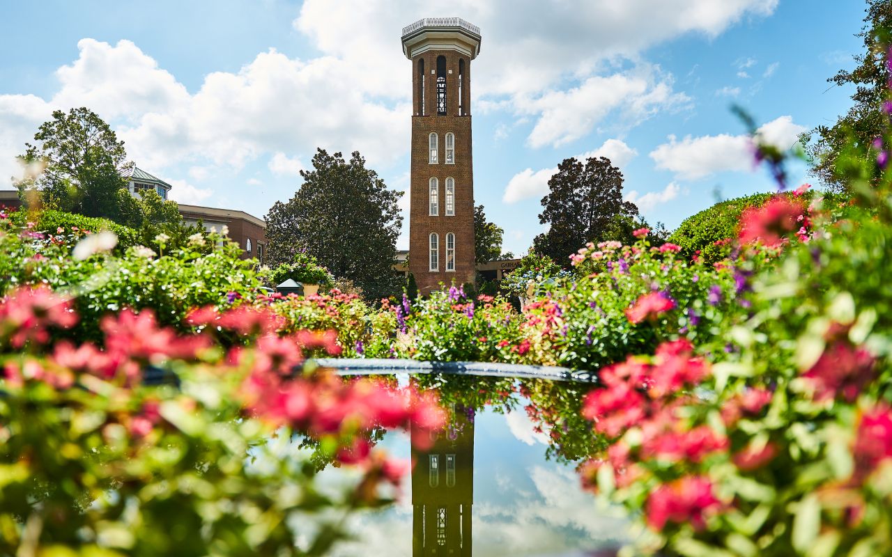 Belmont's Bell Tower surrounded be flowers with a reflection in a fountain