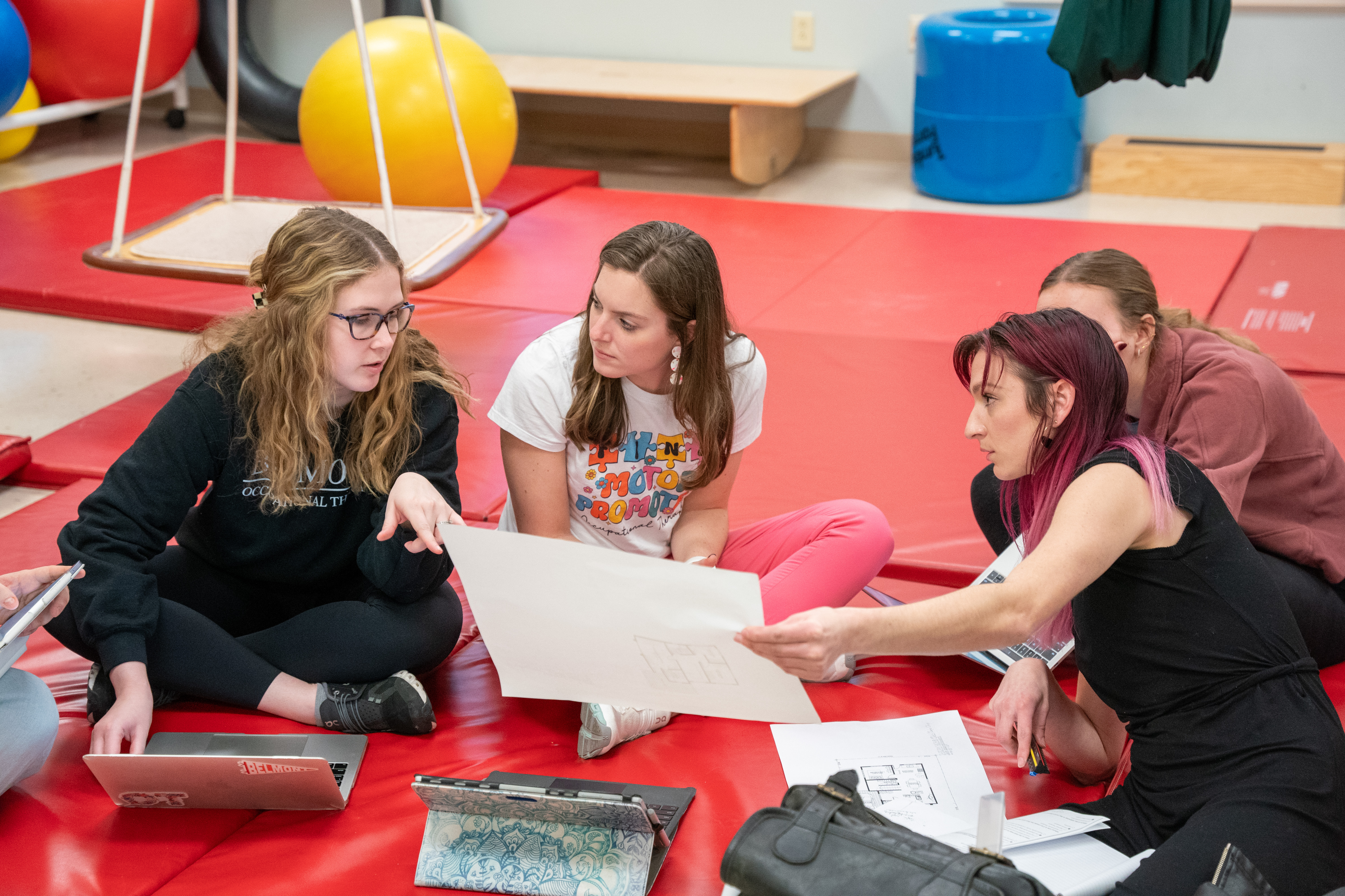 OT and O'More students sit on a mat and discuss the project together