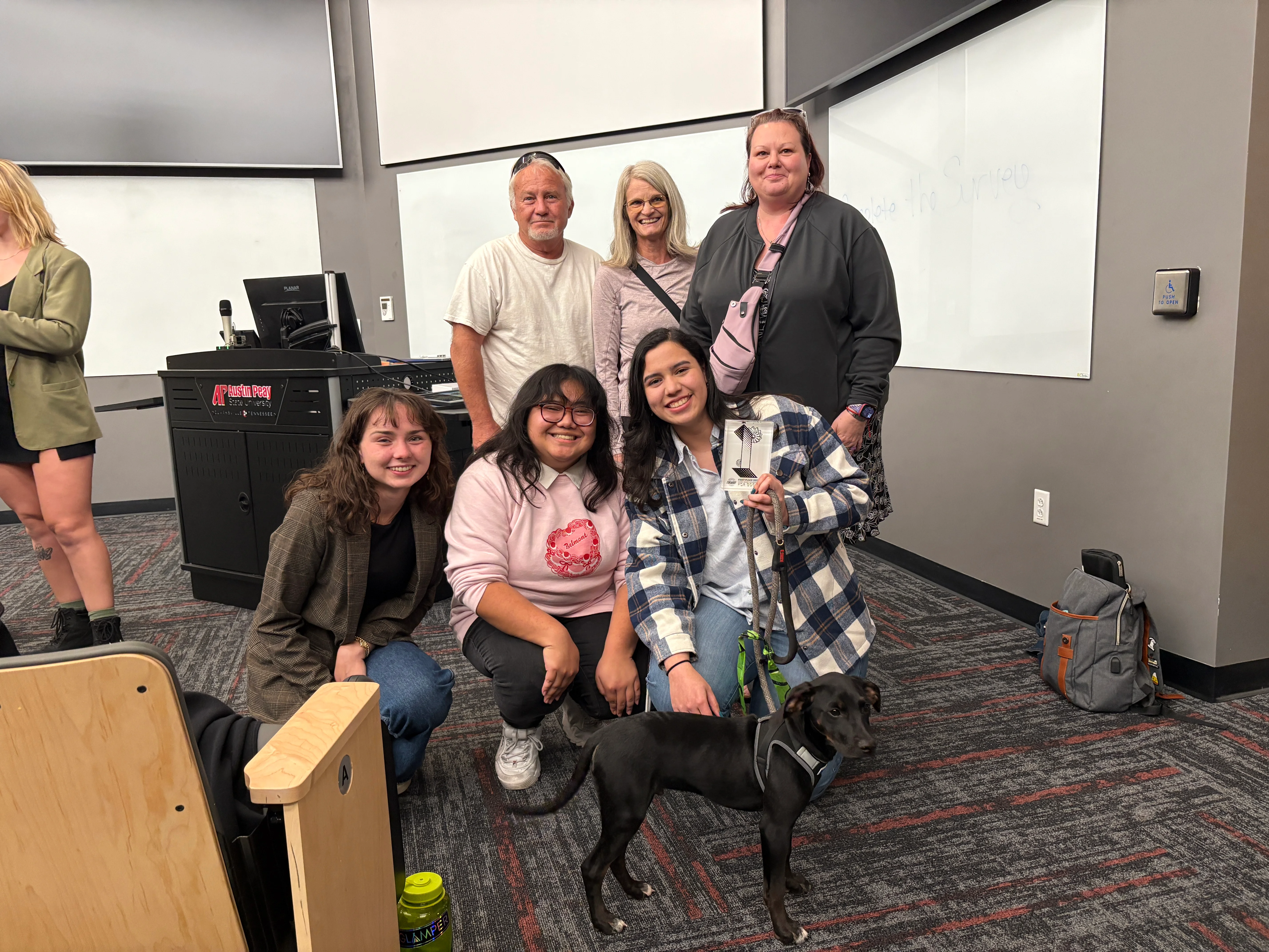 Group of students posing with a black dog.