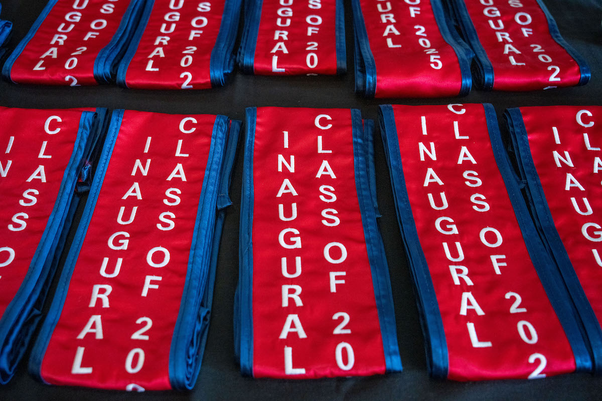 Close-up of red and blue graduation stoles embroidered with “Inaugural Class of 2025” laid out on a table.