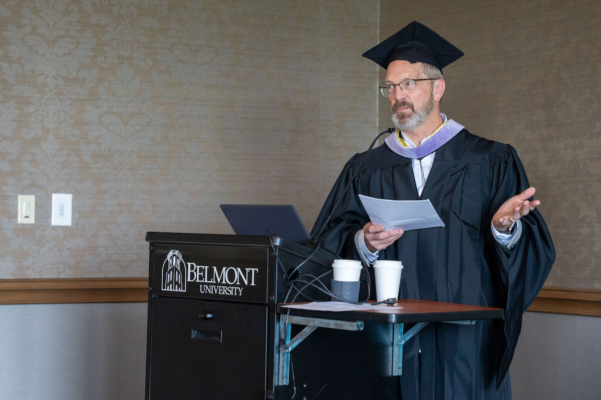 Faculty member in regalia speaks at a Belmont University podium during a graduation ceremony or honors event.