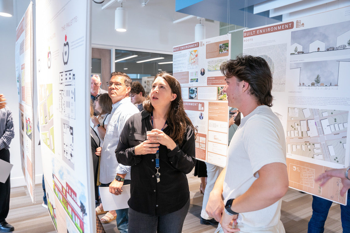 Students and guests view detailed architecture presentation boards during a studio exhibit or final project review.