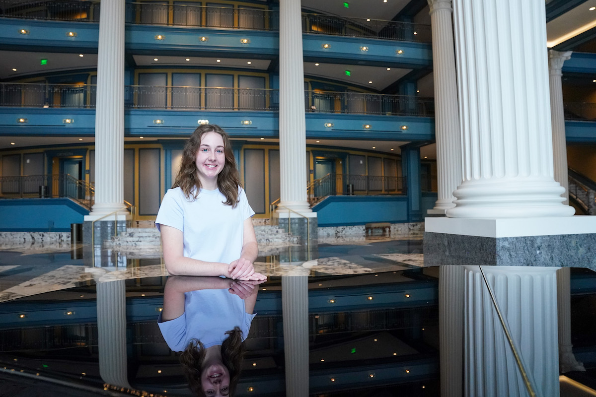 Olivia Hobbs poses inside the Fisher Center for the Performing Arts, reflected on a glossy black piano.