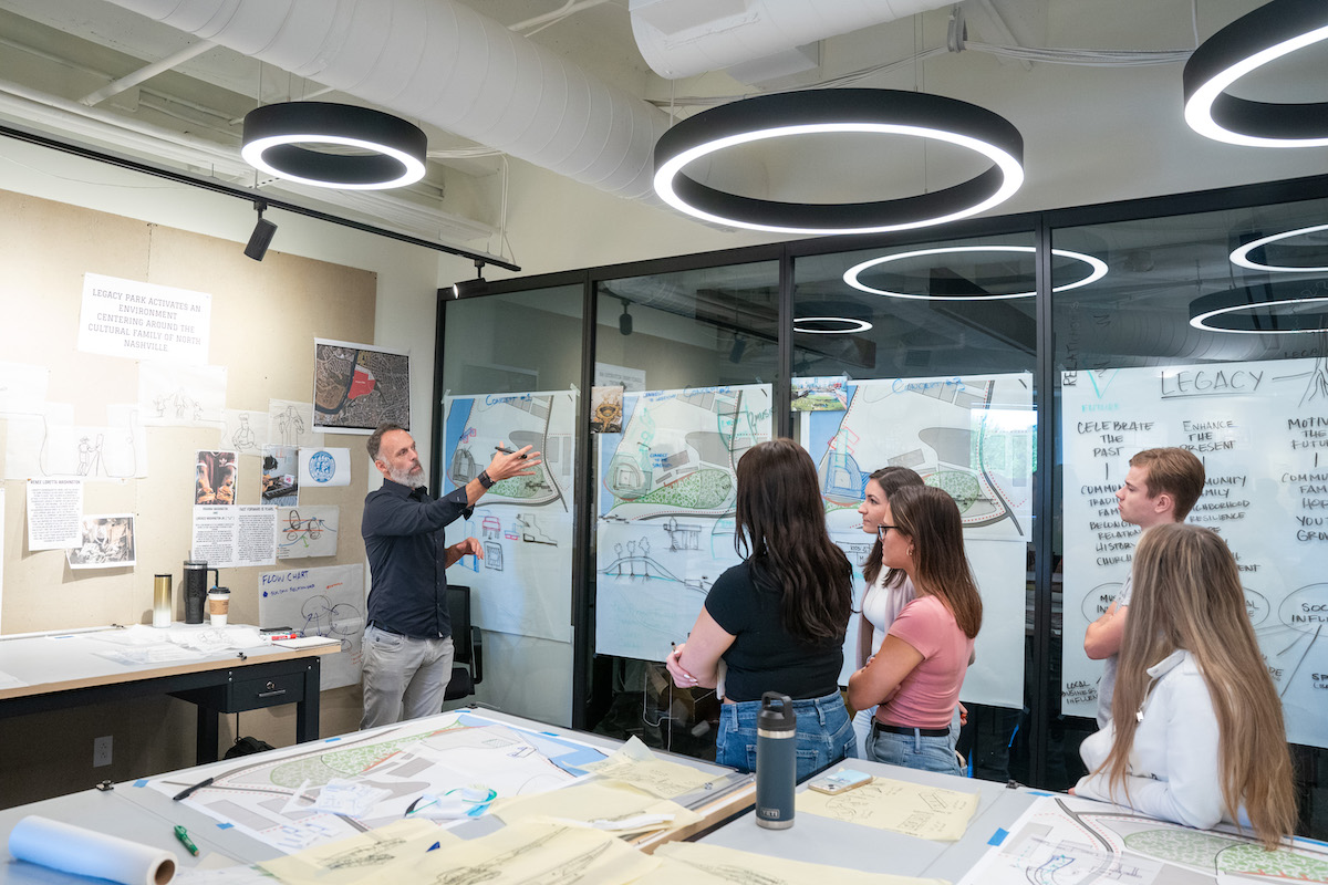 Group discussion about concept boards and sketches displayed across a studio workspace wall.
