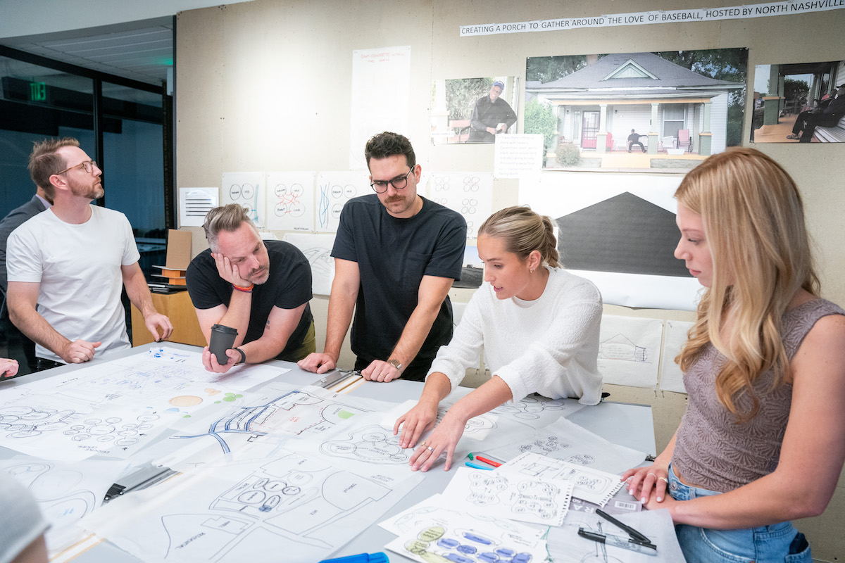 Architecture students engage in critique and discussion with visiting reviewers in a classroom filled with sketches and diagrams.