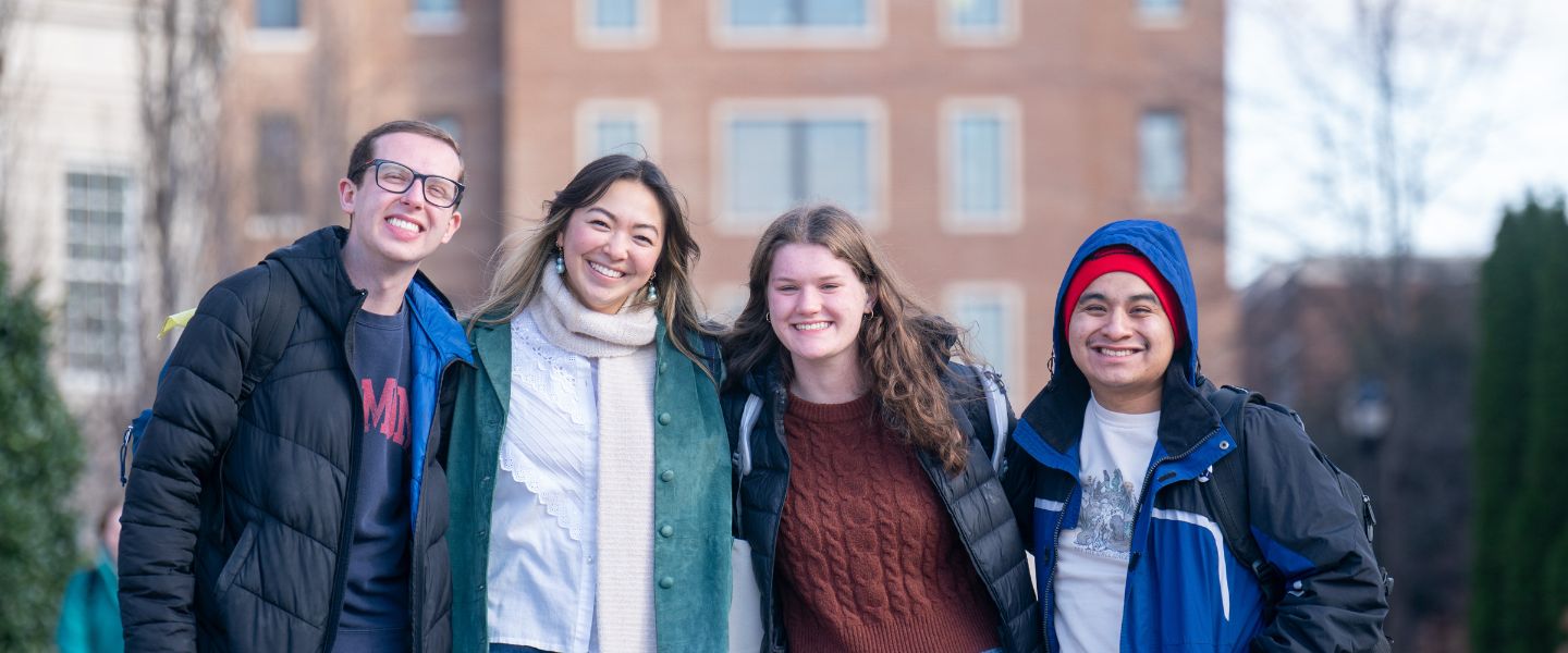 Four students stand outside and smile