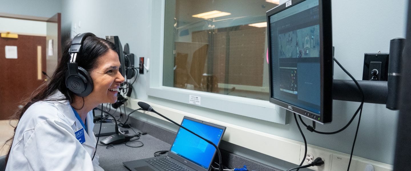 Woman in lab coat smiles in front of computer