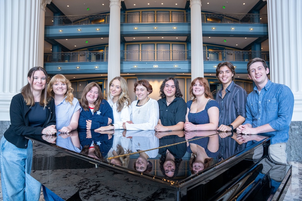 Dolly fellows pose for group photo at a piano in the Fisher Center