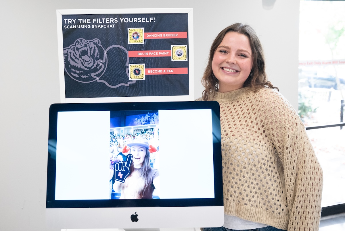 student smiles with computer screen showing filters for snapchat