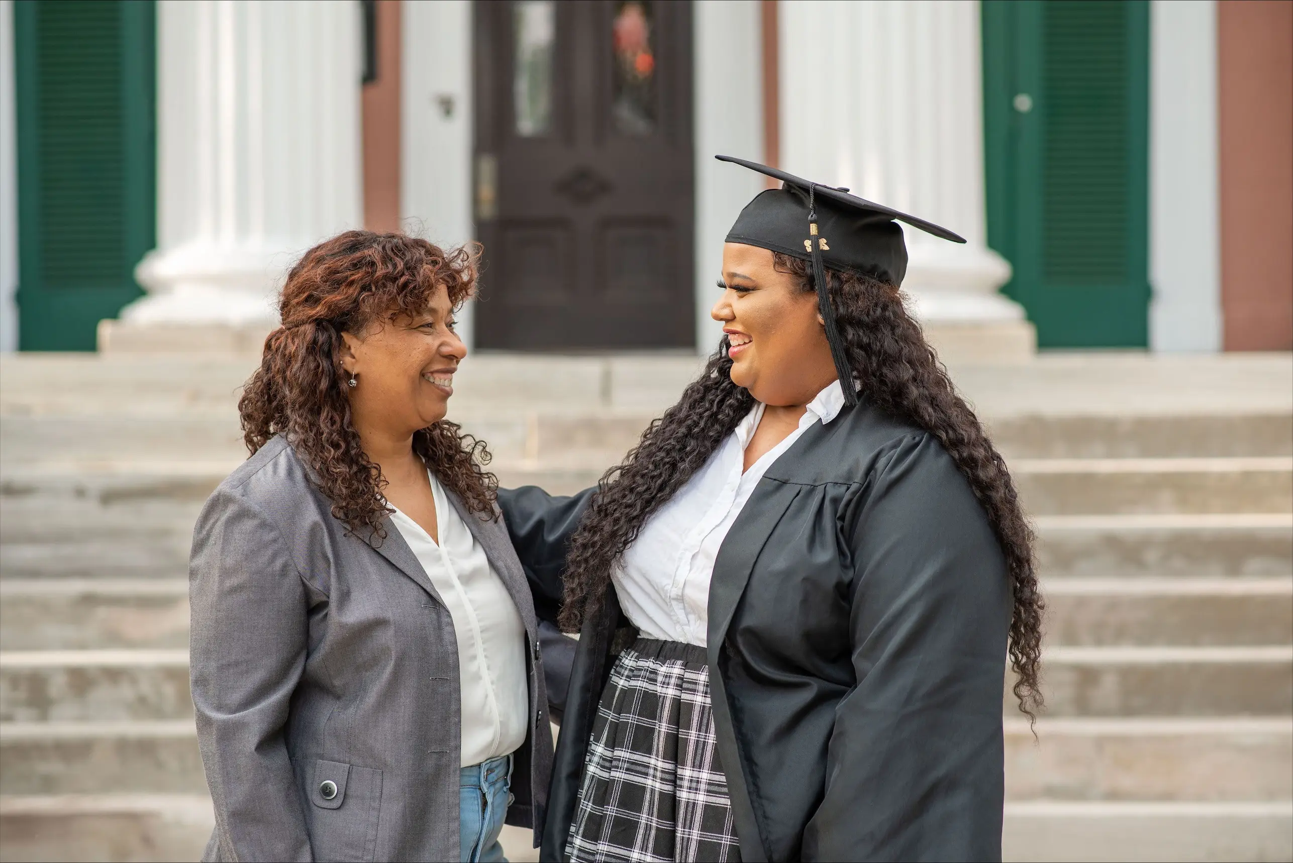 O'More alumna Janet Reyes shares a joyful moment in graduation attire with her mom outside.