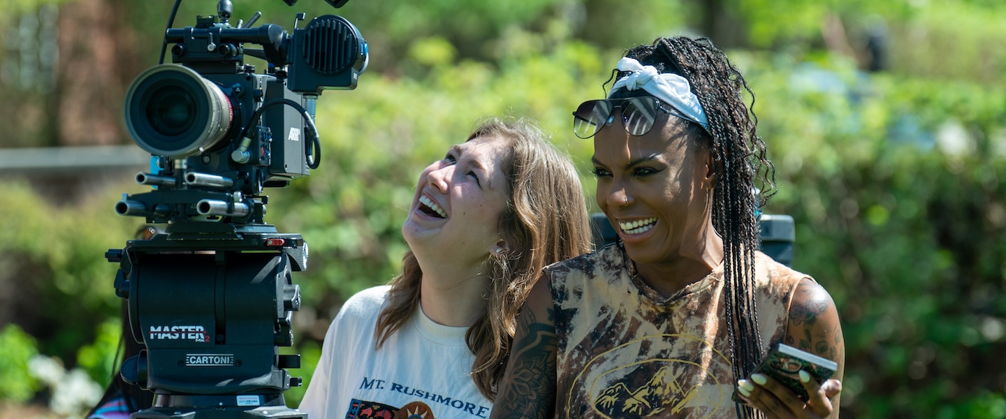 Two Belmont film students smile and laugh while working with a professional-grade camera during an outdoor film shoot.
