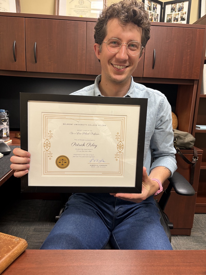 Patrick Riley holding "Most Likely to be a Law School Professor" certificate in his Belmont office
