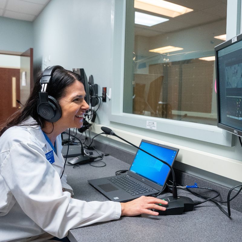 Woman in lab coat smiling at computer