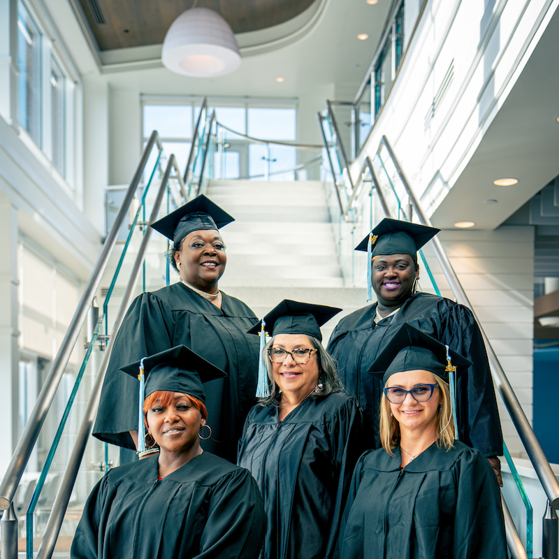 Five female graduates on stairs with caps and gownsAlt Text