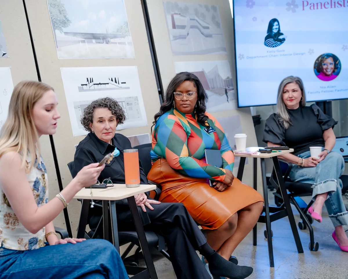 A student moderates a Women’s History Month panel at Belmont’s O’More College, joined by faculty and industry professionals seated in front of design boards and a presentation screen.