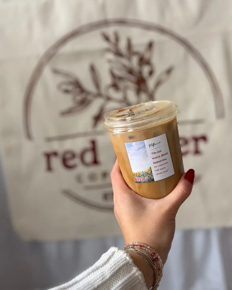 Someone's hand holding a coffee cup with Bible scripture in front of a banner