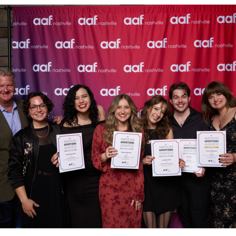 Smiling team celebrating American Advertising Awards, holding certificates against an AAF Nashville banner.