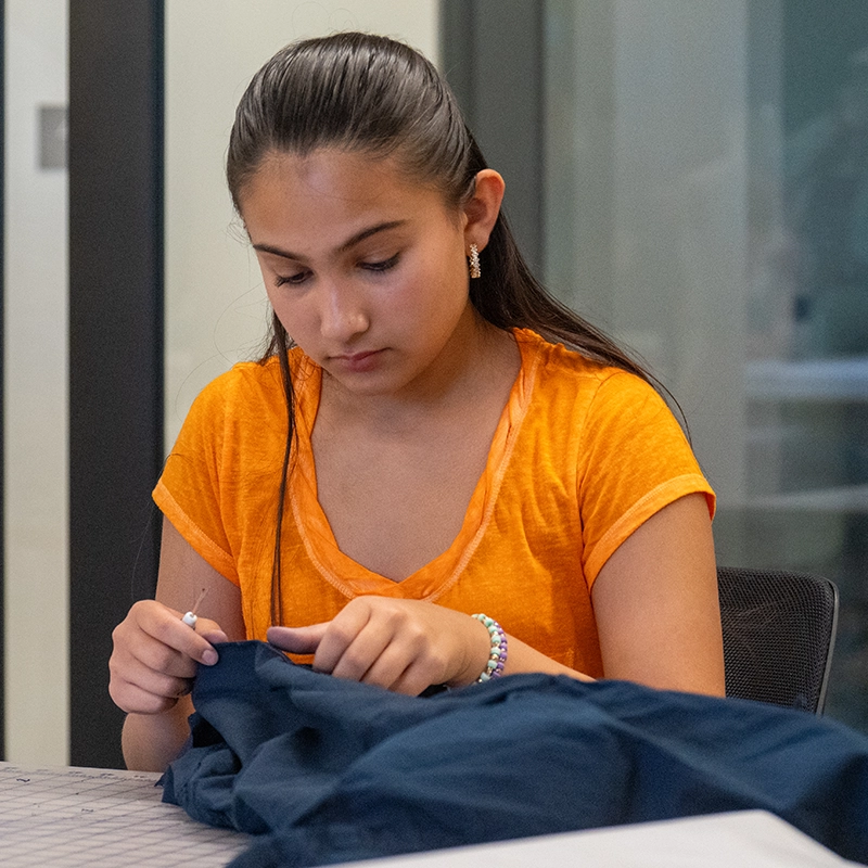 A young girl in an orange shirt is working on blue fabric.