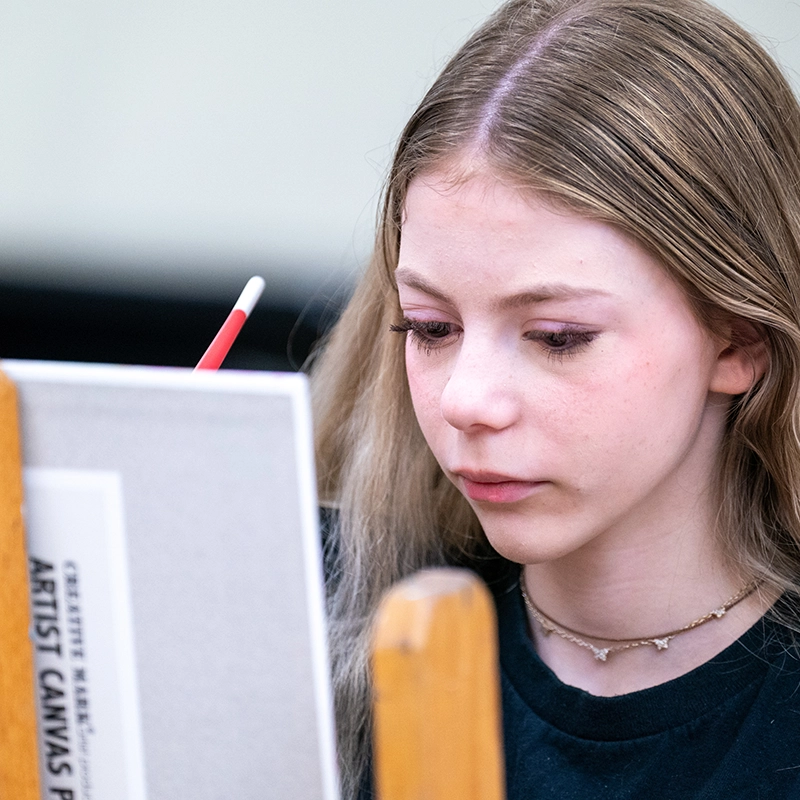 A young girl works on a canvas with a paint brush