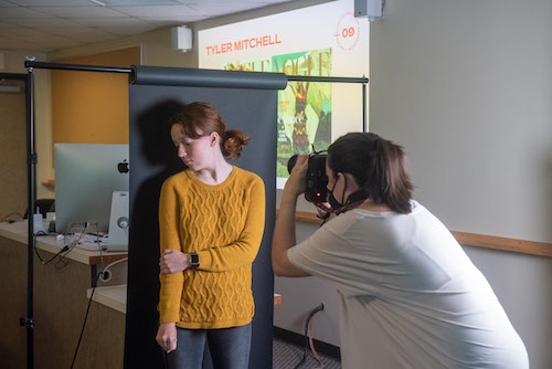 Students taking a photo of a model in front of a backdrop