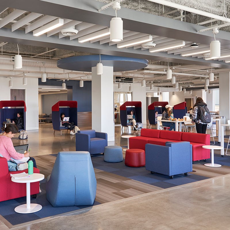 Interior view of a modern, open study and lounge area at Belmont University, featuring comfortable seating, individual study pods, and students working on laptops.