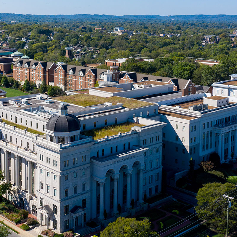 Aerial view of Belmont University's campus, showcasing the Janet Ayers Academic Center and surrounding buildings, with a backdrop of lush greenery and distant hills.