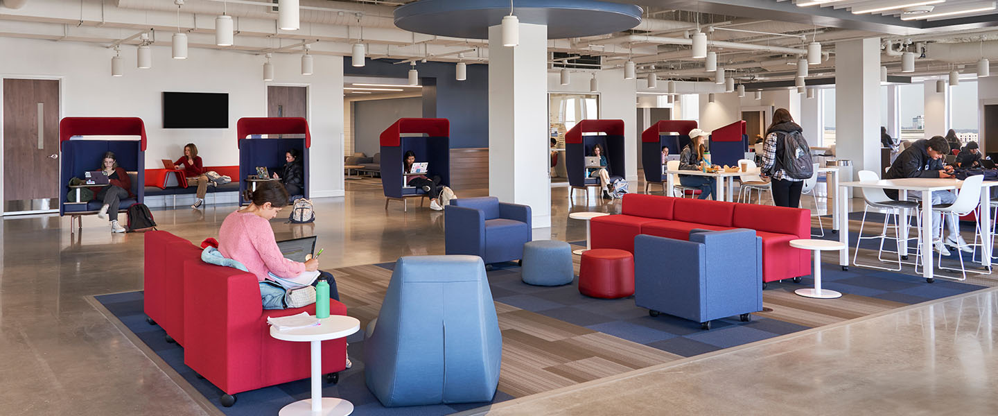 Interior view of a modern, open study and lounge area at Belmont University, featuring comfortable seating, individual study pods, and students working on laptops.