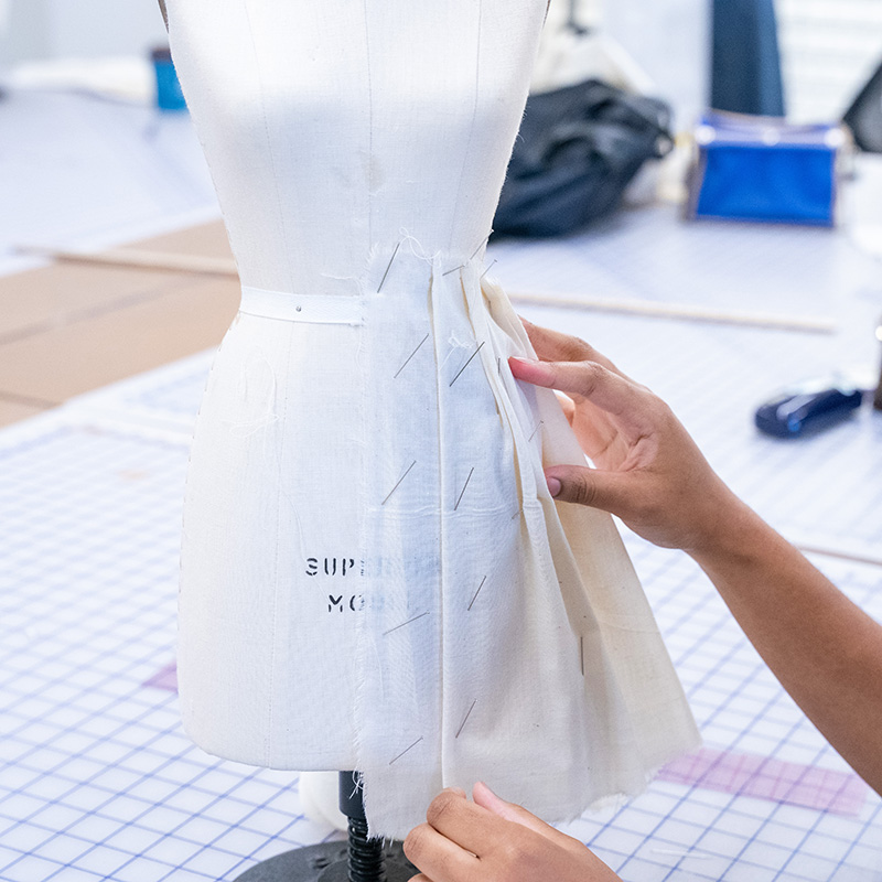 A student pins drapery onto a dressform