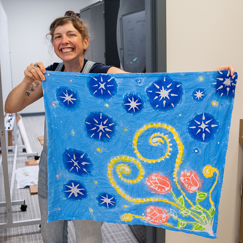 Woman holding up a blue cloth with yellow and blue swirly patterns on it. 