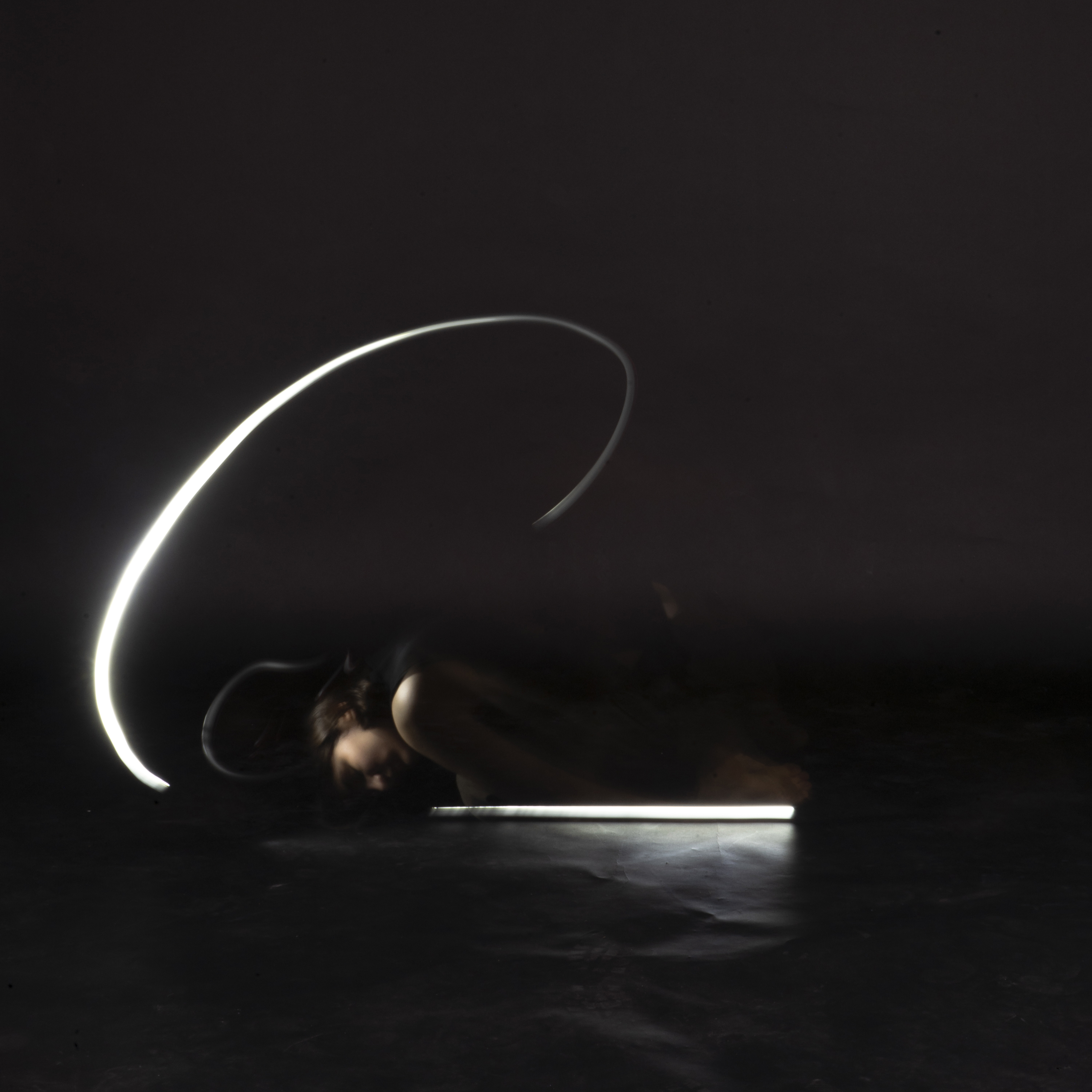 person in darkness crouched down on floor with light swirl around