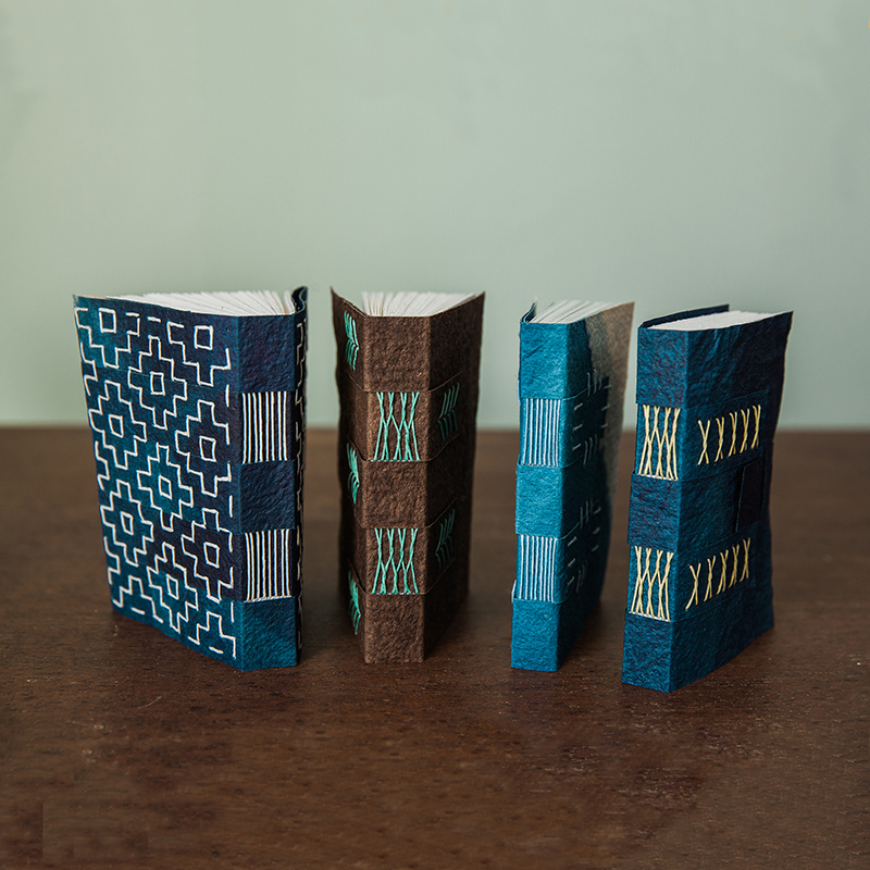 Four handmade books lined up with the spine showing decorative stitching
