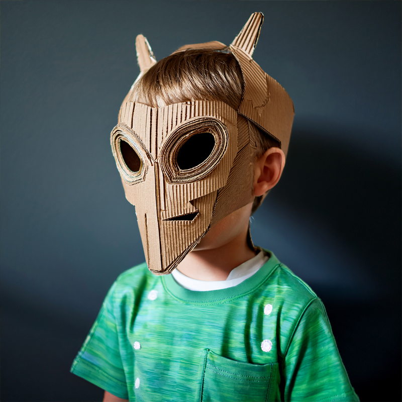 Image of a kid standing at three-quarter view with a cardboard alien mask on. 