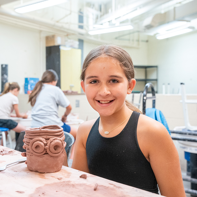 Kid sitting next to a ceramic pot smiling