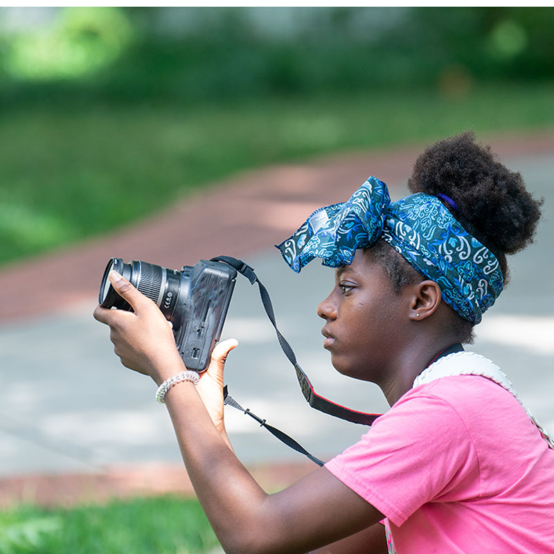 student holding a digital camera looking through the lens 