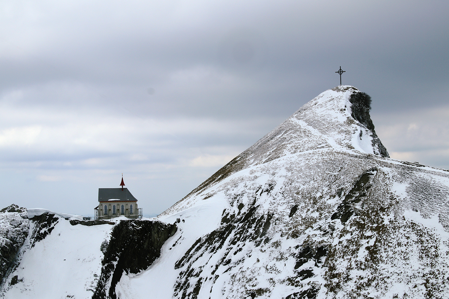 Landscape shot of snow covered mountains with a church and an cross