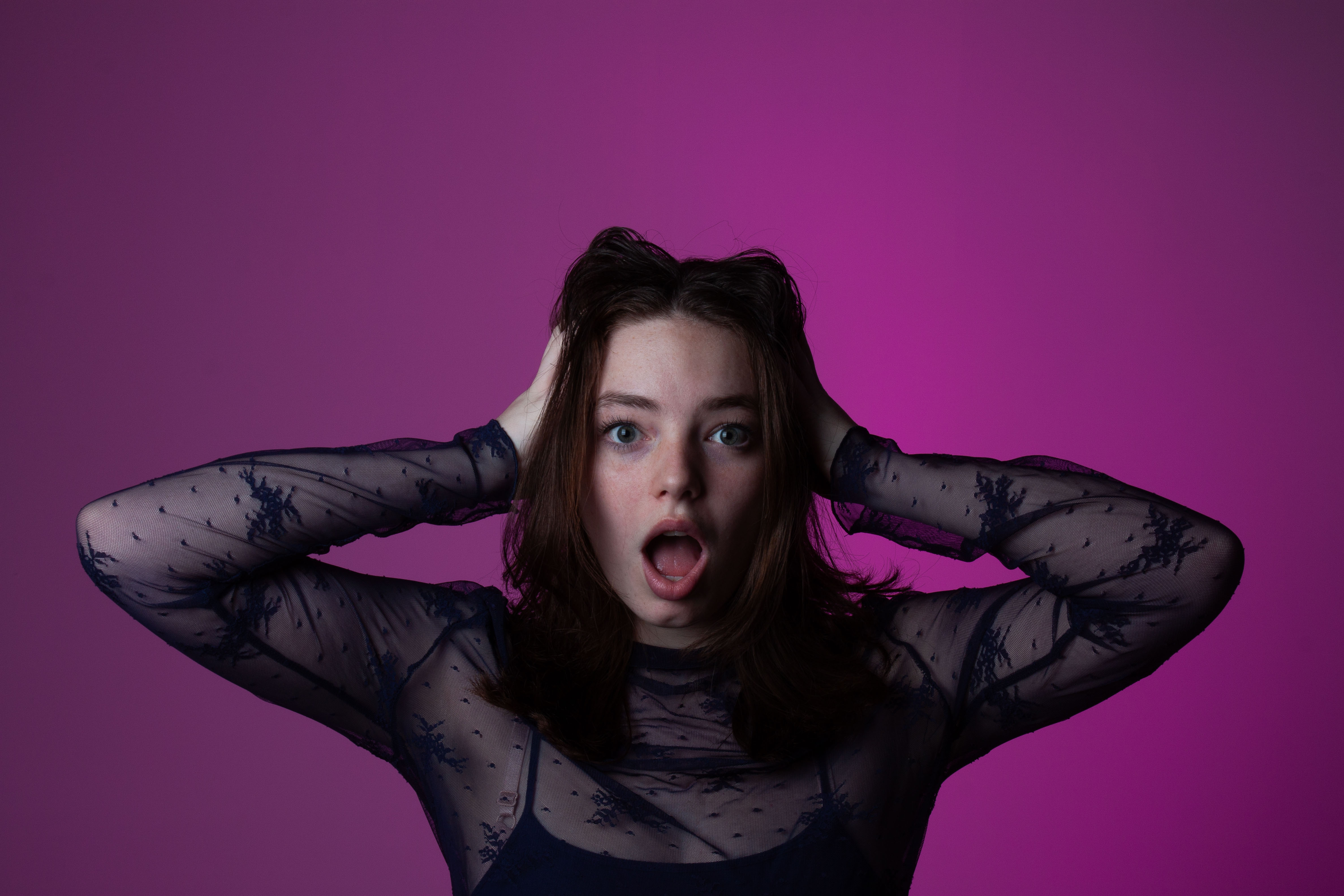 Girl with her hands on her head and mouth open in front of a purple background