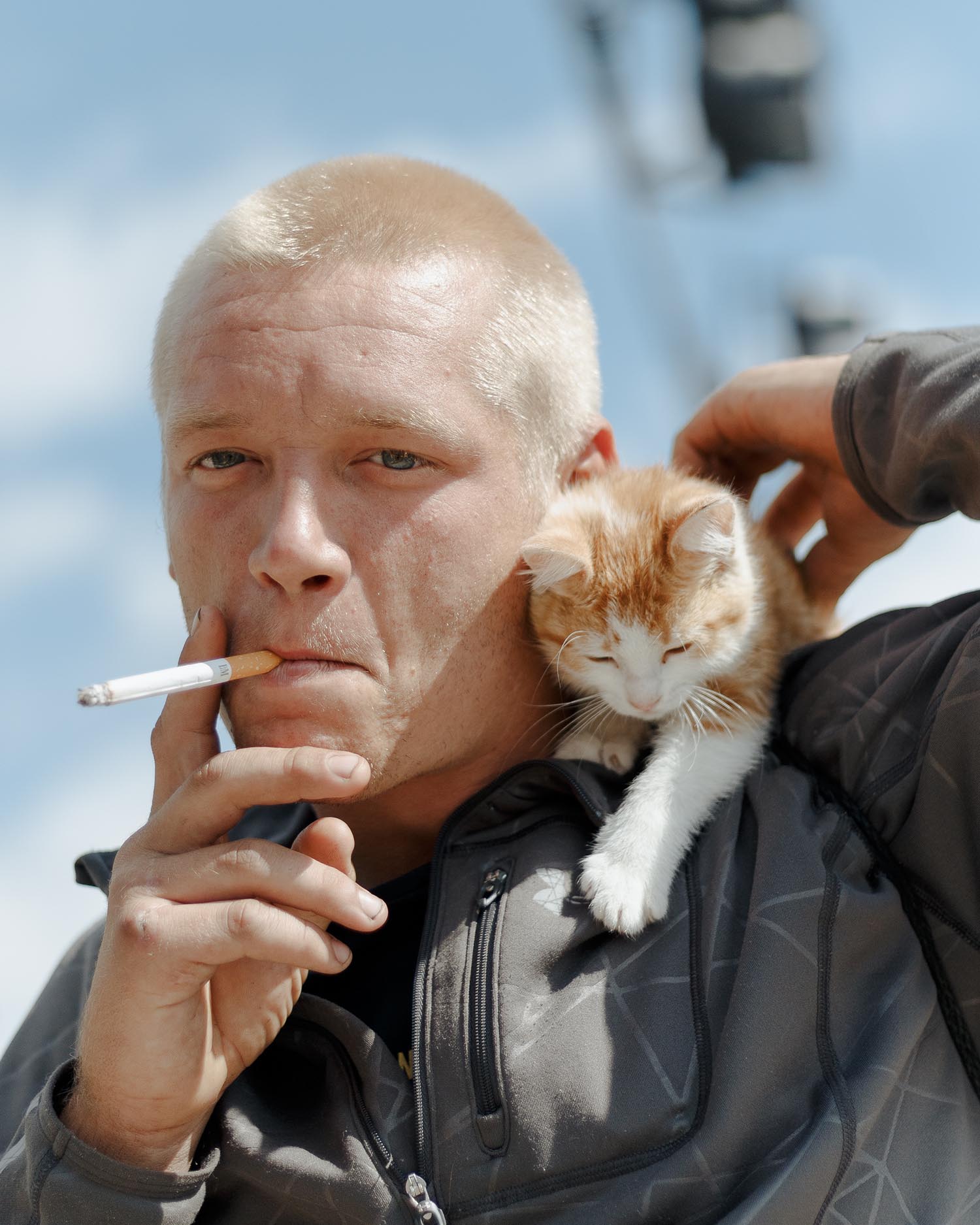 man in leather jacket smoking while a white and orange kitten sits on him shoulder